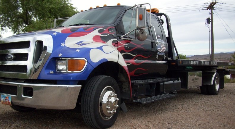 A black Freedom Towing tow truck with red, white, and blue flames and stars