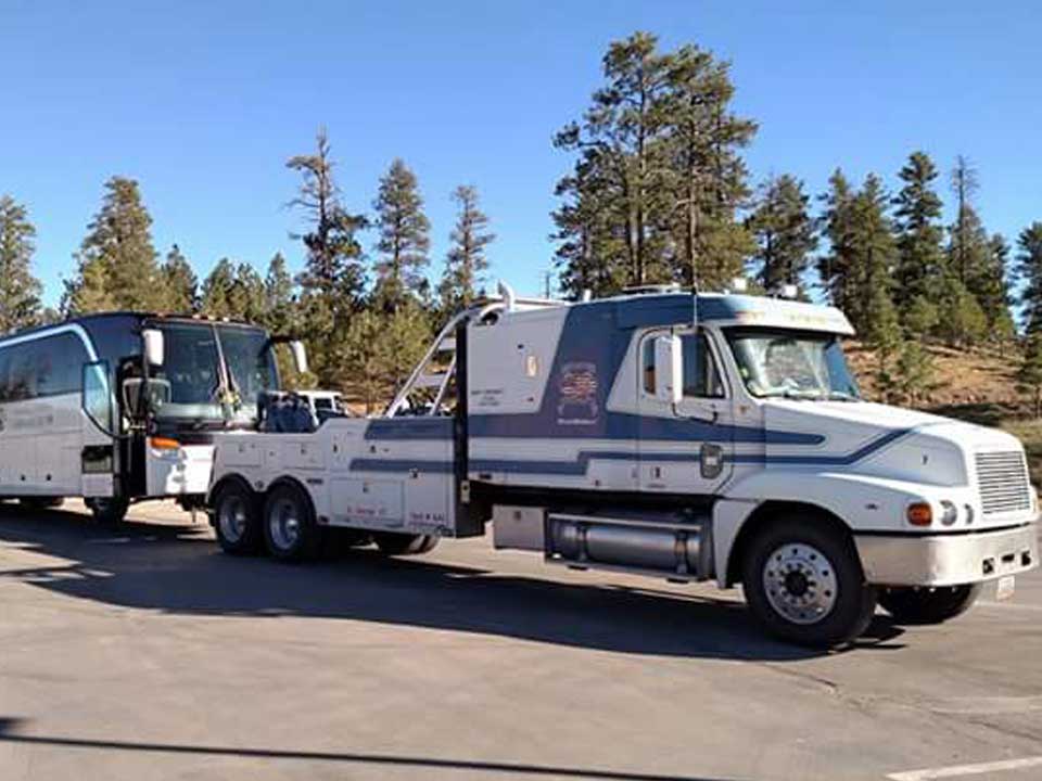 A blue and white Freedom Towing tow truck tows a white semi