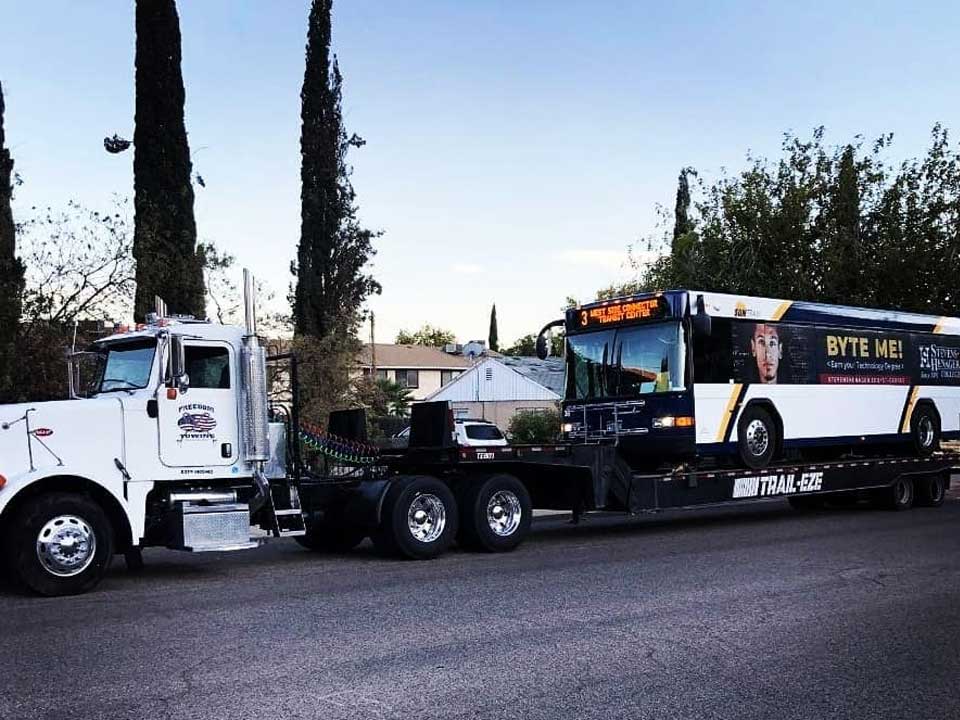 a white Freedom Towing hauler towing a city bus